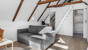 A modern loft bedroom with exposed wooden beams, a grey sofa, a small table, and a staircase leading to a kitchen. - "Ilona" - 2km from the sea by Interhome (Rømø)