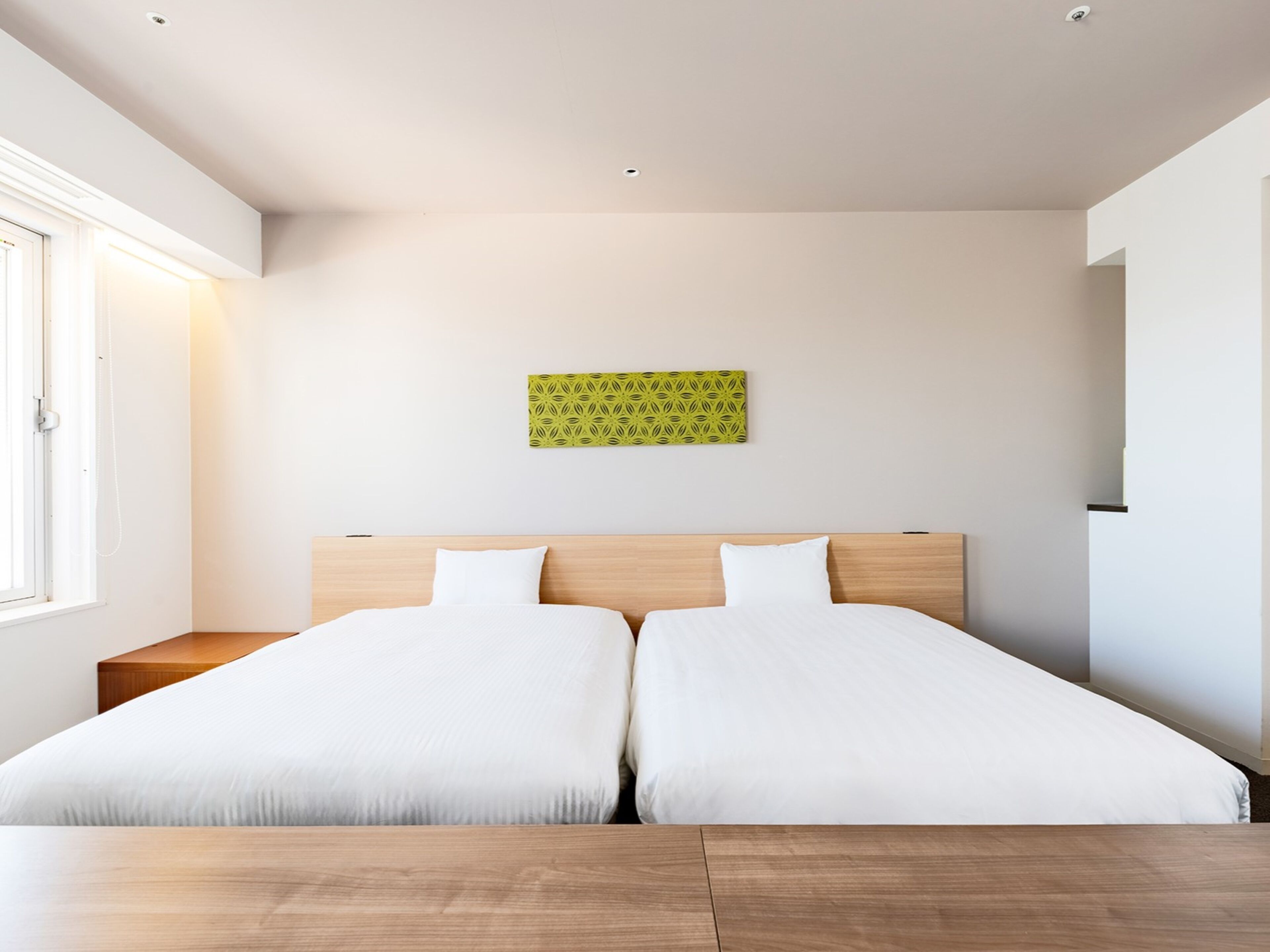 A modern hotel room with a large bed, wooden headboard, and a green patterned wall decoration.