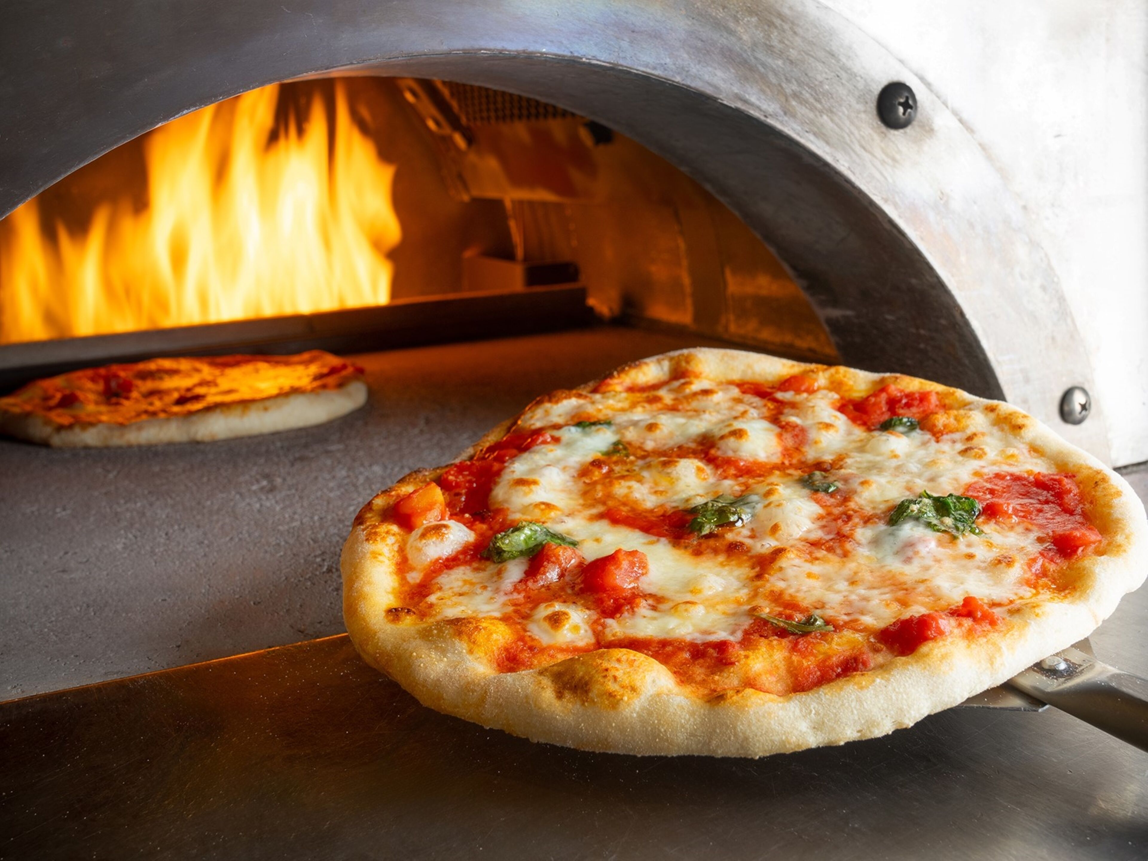 Un horno de pizza con dos pizzas en cocción.