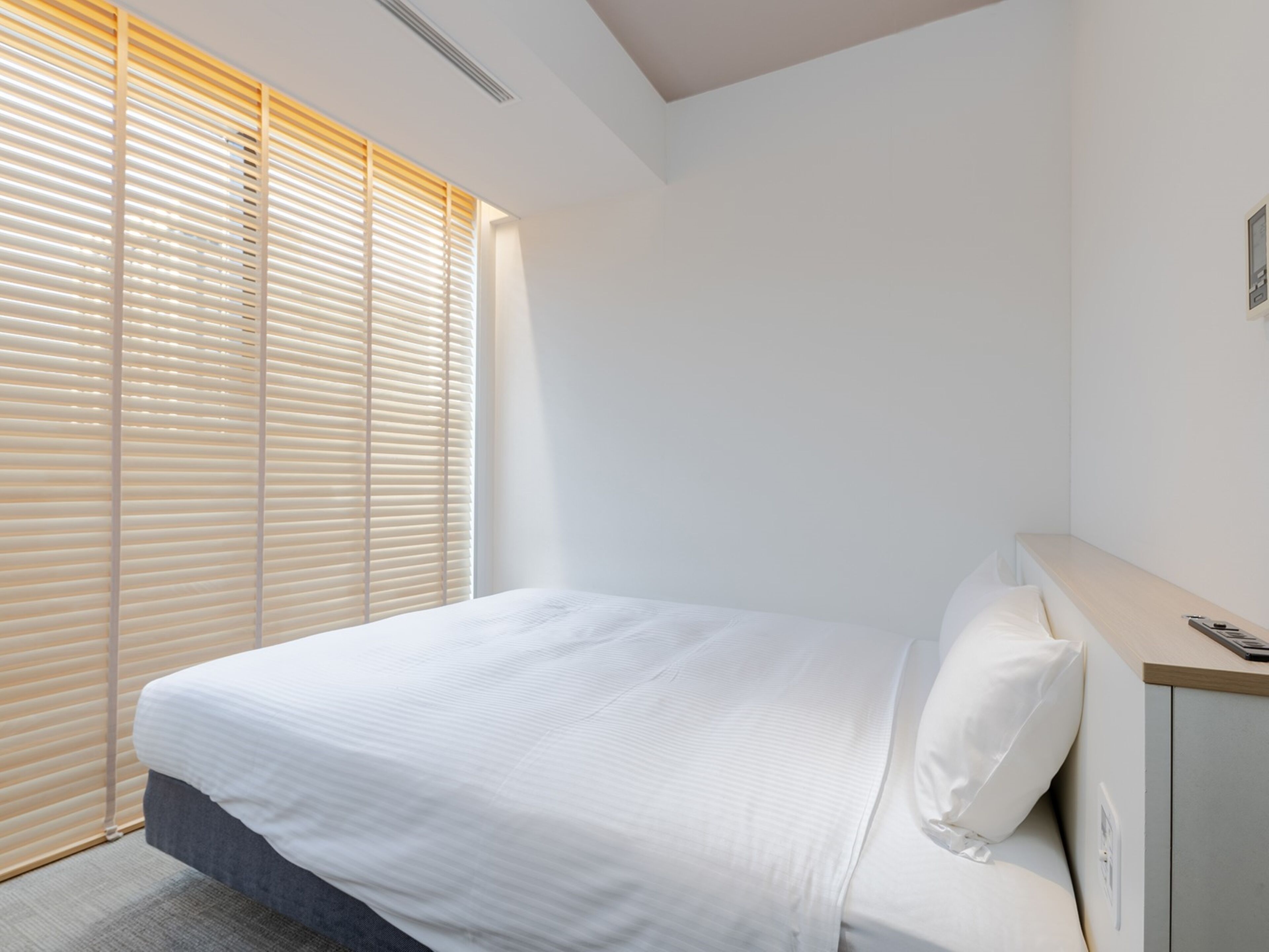 Una habitación de hotel moderna con una cama grande, una mesita de noche y una ventana con persianas.