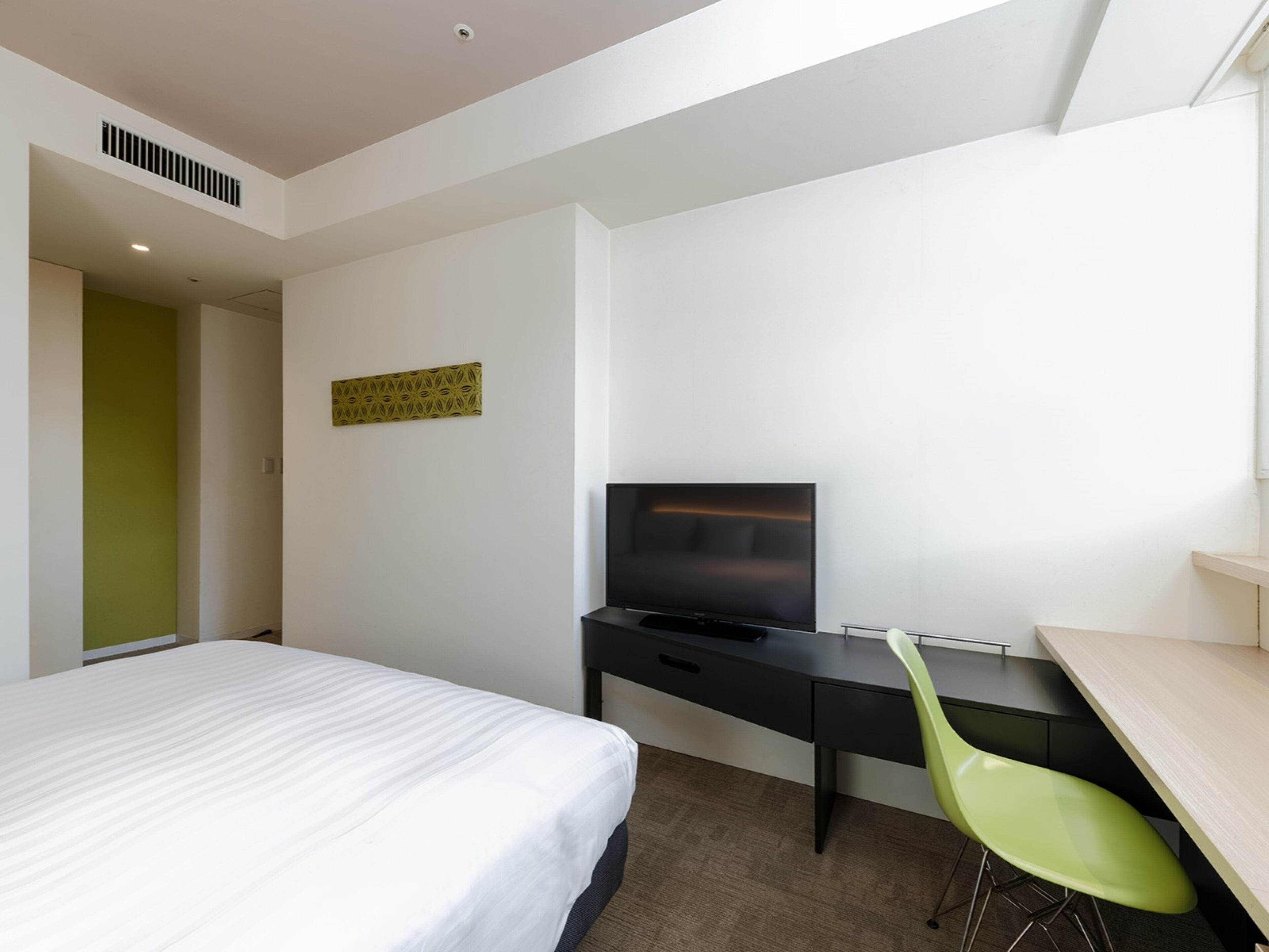 Una habitación de hotel con una cama, un escritorio con televisor y una silla verde.