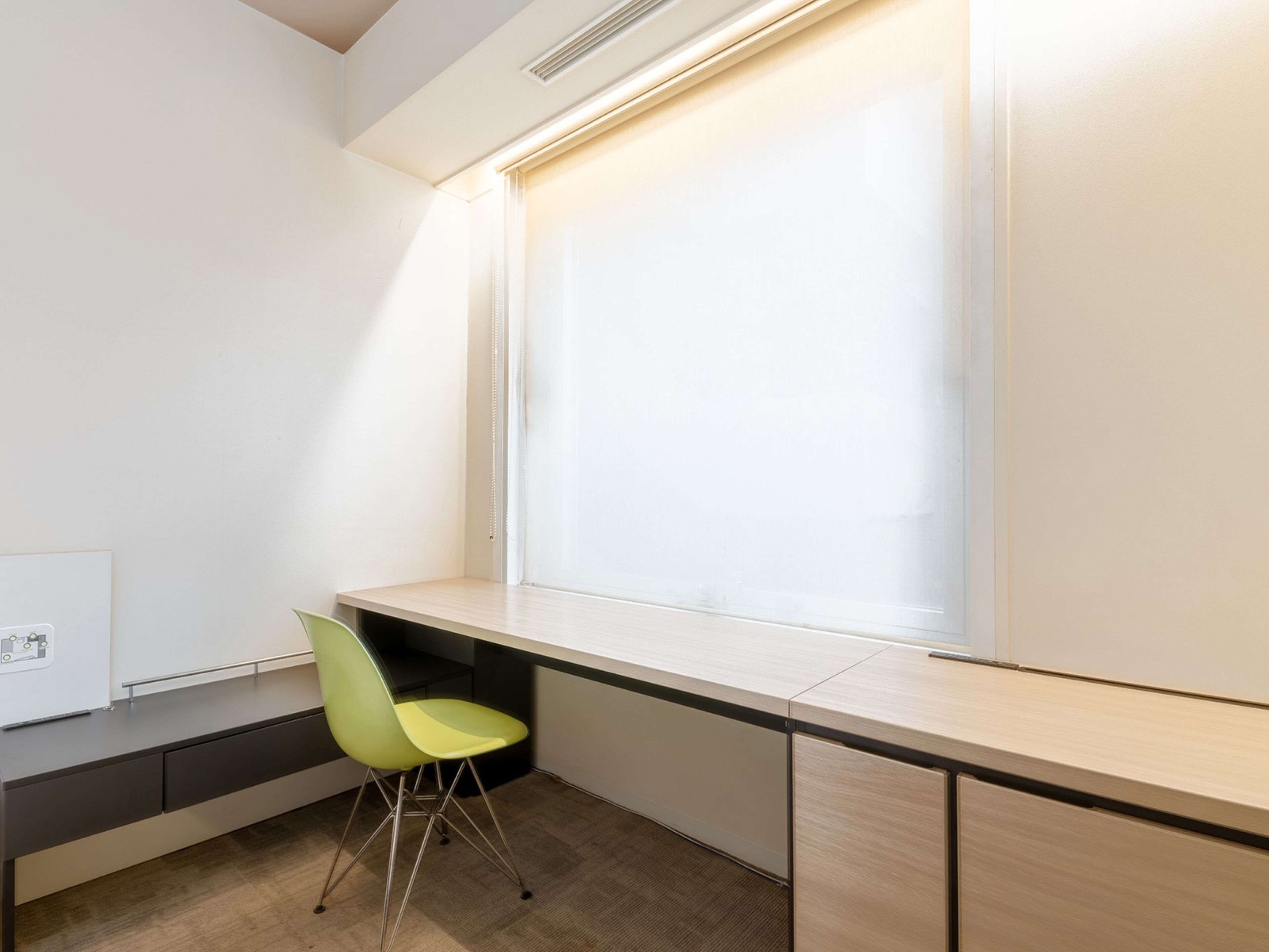 Ein moderner Arbeitsraum mit Schreibtisch, grünem Stuhl und Fenster mit Jalousien.