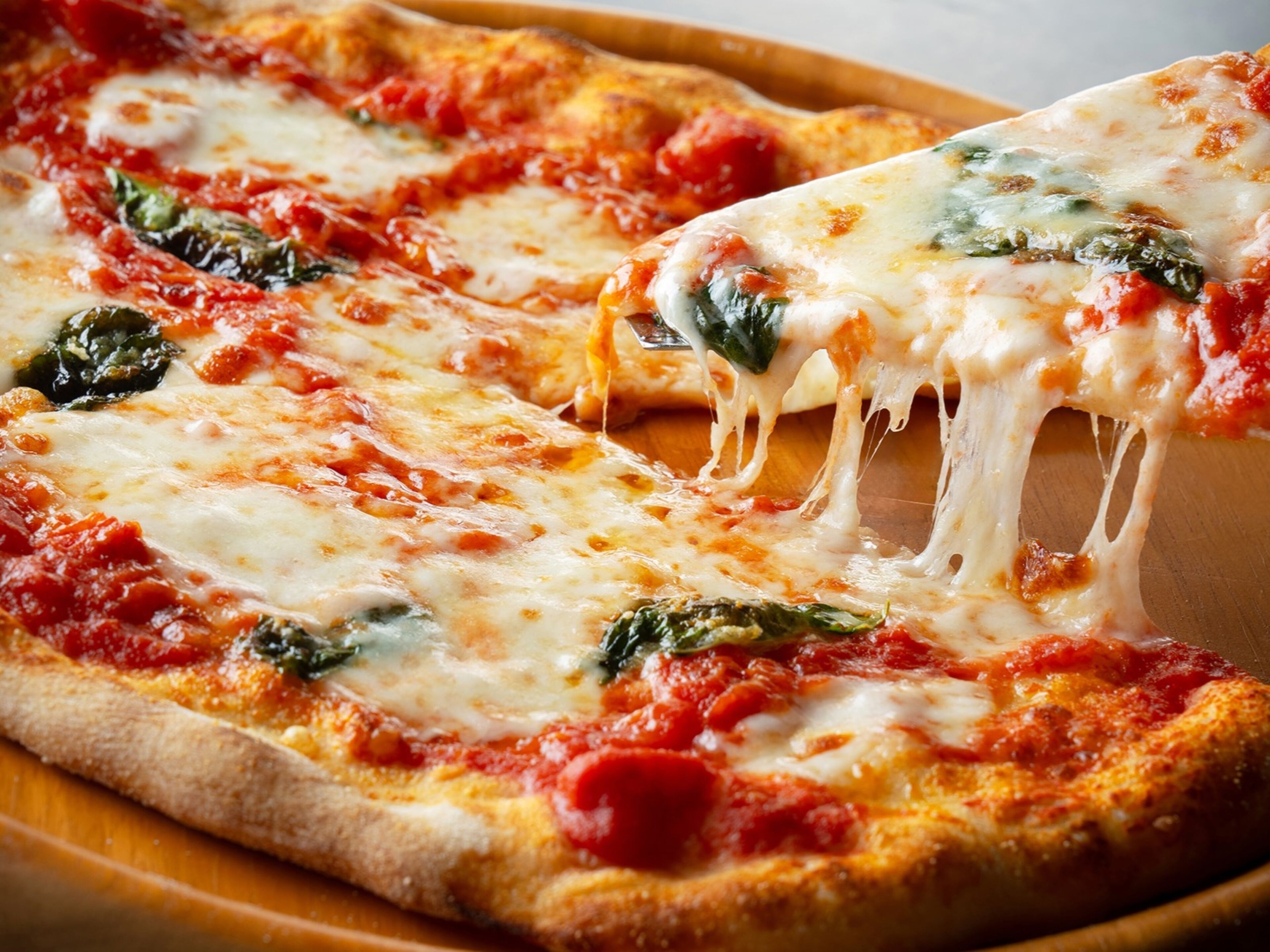 A pizza with melted cheese and spinach on a wooden board.