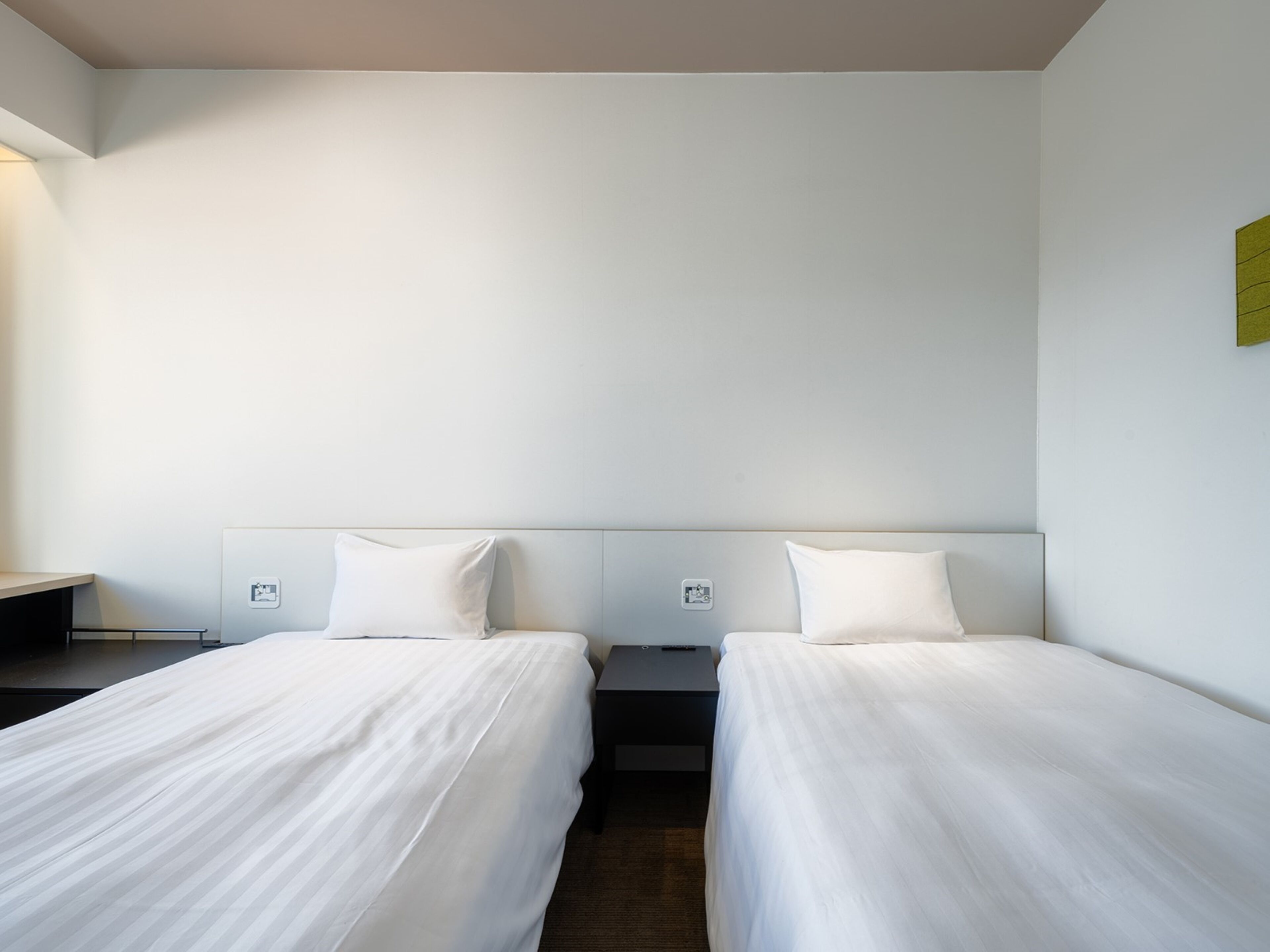 A hotel room with two single beds, a small bedside table, and a wall-mounted light fixture.