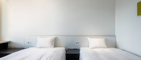 Una habitación de hotel con dos camas individuales, una mesita de noche pequeña y una lámpara fijada a la pared.