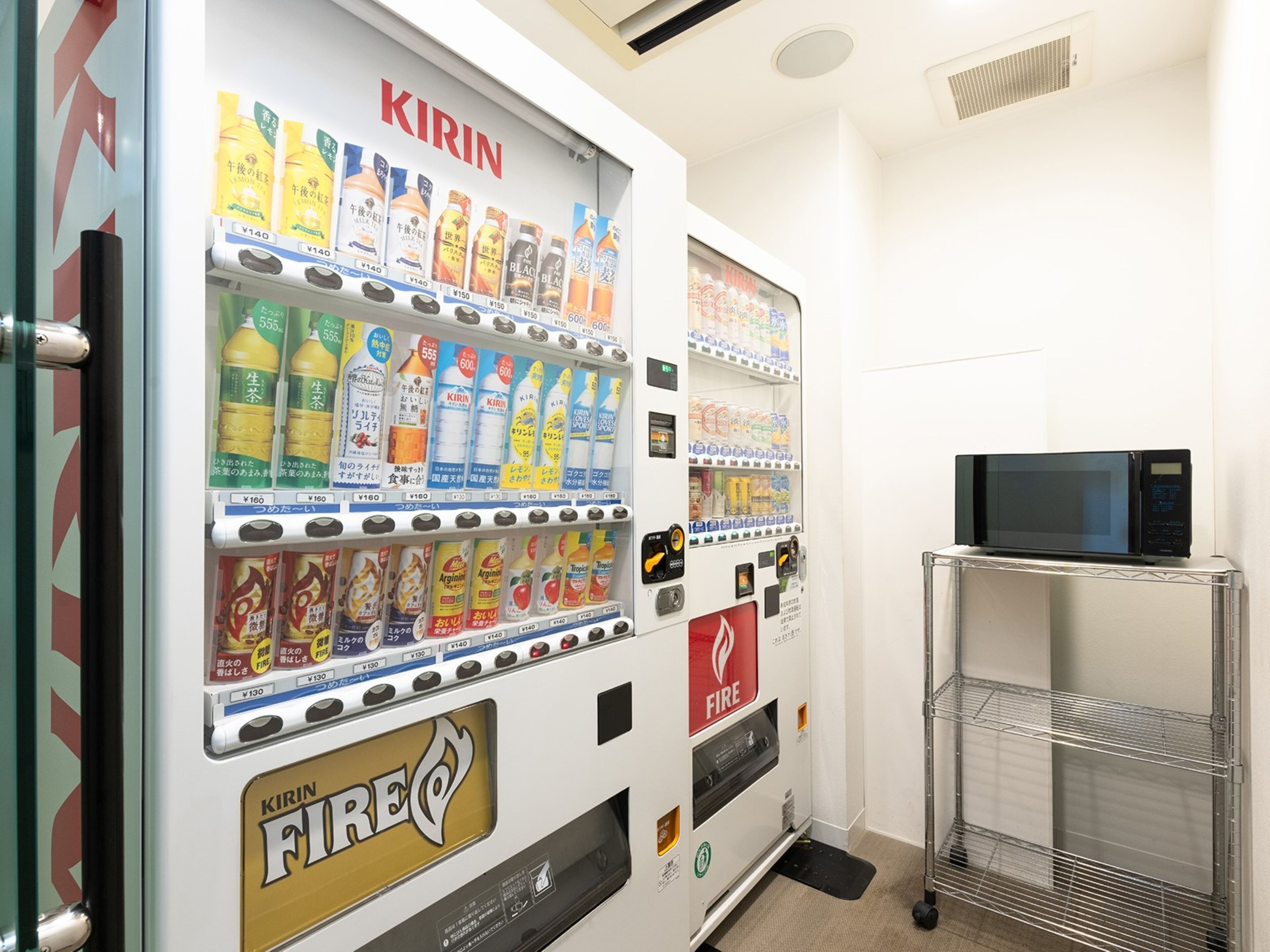 A vending machine with various beverages and snacks, a fire extinguisher, and a microwave on a shelf.