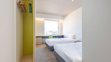 A modern hotel room with two beds, a window with a city view, a desk, and a green wall.