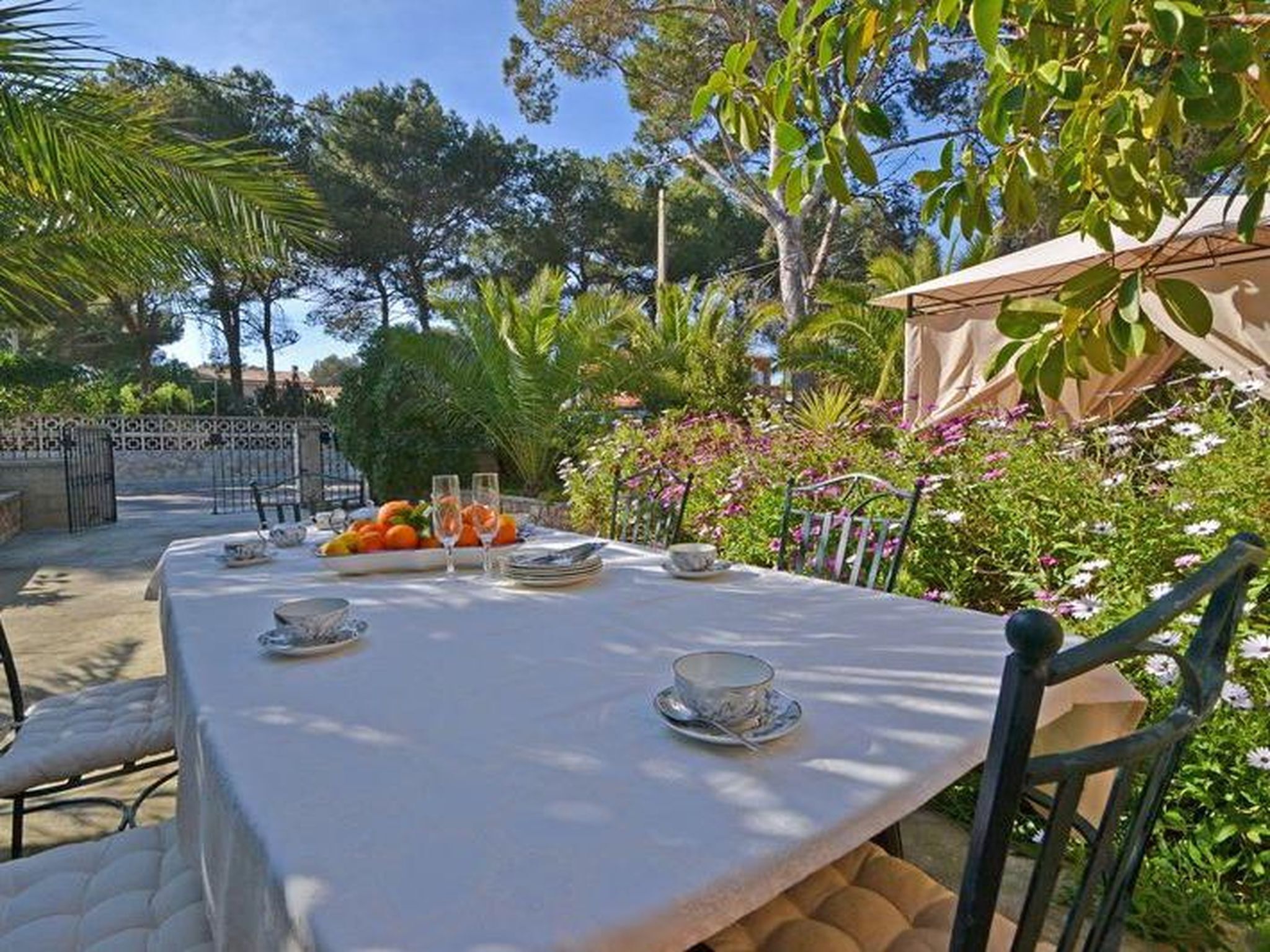 Un espace de restauration en plein air avec une table dressée pour deux personnes, entouré d’une végétation luxuriante et de fleurs.