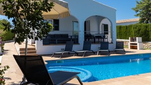 A modern outdoor pool area with a white building, outdoor seating, and a clear blue pool. - Villas Finesse Type 1 by Interhome (Son Bou)