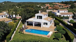 A modern villa with a swimming pool, surrounded by lush greenery and a hilly landscape.