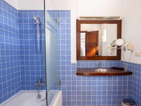 A bathroom with blue tiled walls, a glass shower enclosure, a wooden vanity with a sink, and a mirror with a light.