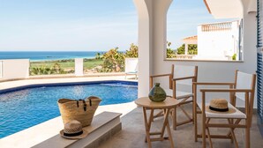 A poolside area with a view of the ocean, a table with chairs, and a large woven basket. - Villa Atalis by Interhome (Son Bou)