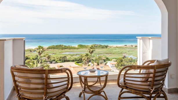 A balcony with two wicker chairs and a small table, overlooking a beach and ocean. - Villa Atalis by Interhome (Son Bou)