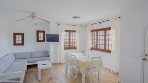 A living room with a sofa, a dining table with chairs, a ceiling fan, and a TV mounted on the wall. - Son Bou Gardens 3 dorm by Interhome (Son Bou)