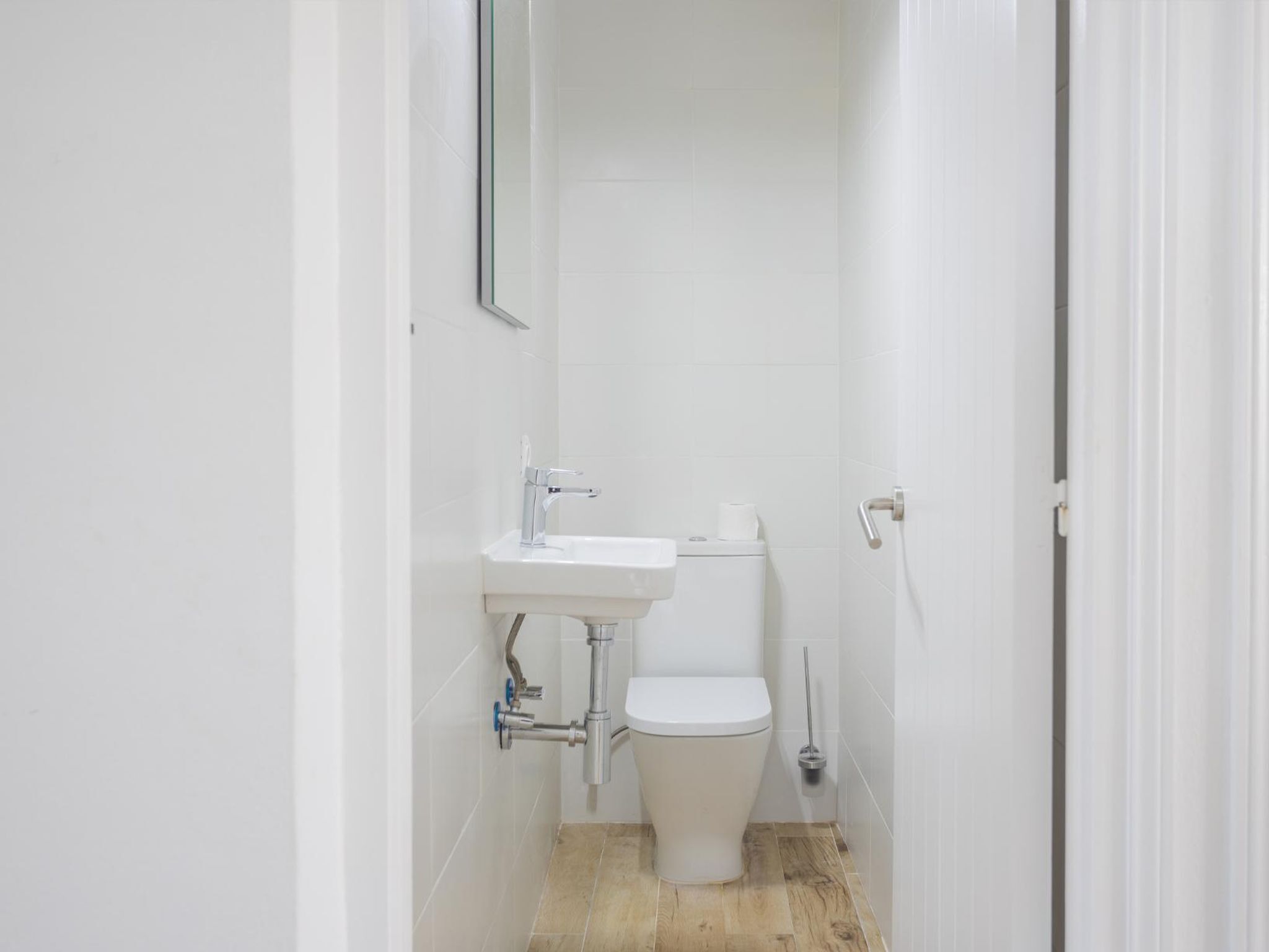 Ein kleines, weißes Badezimmer mit Toilette, Waschbecken und einem Spiegel an der Wand.
