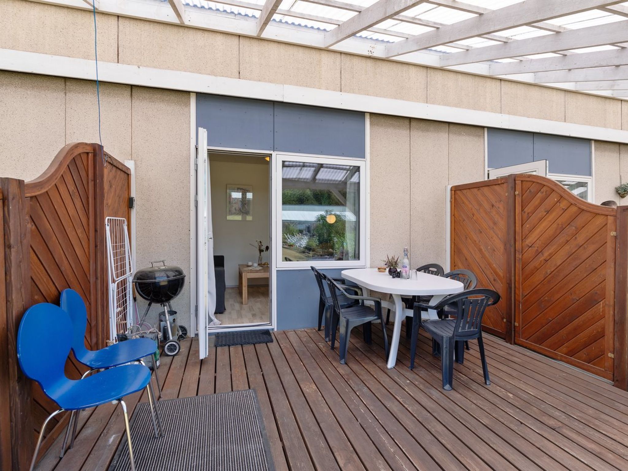 An outdoor patio with a wooden table and chairs, a grill, and a wooden gate.