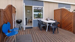 An outdoor patio with a wooden table and chairs, a grill, and a wooden gate.