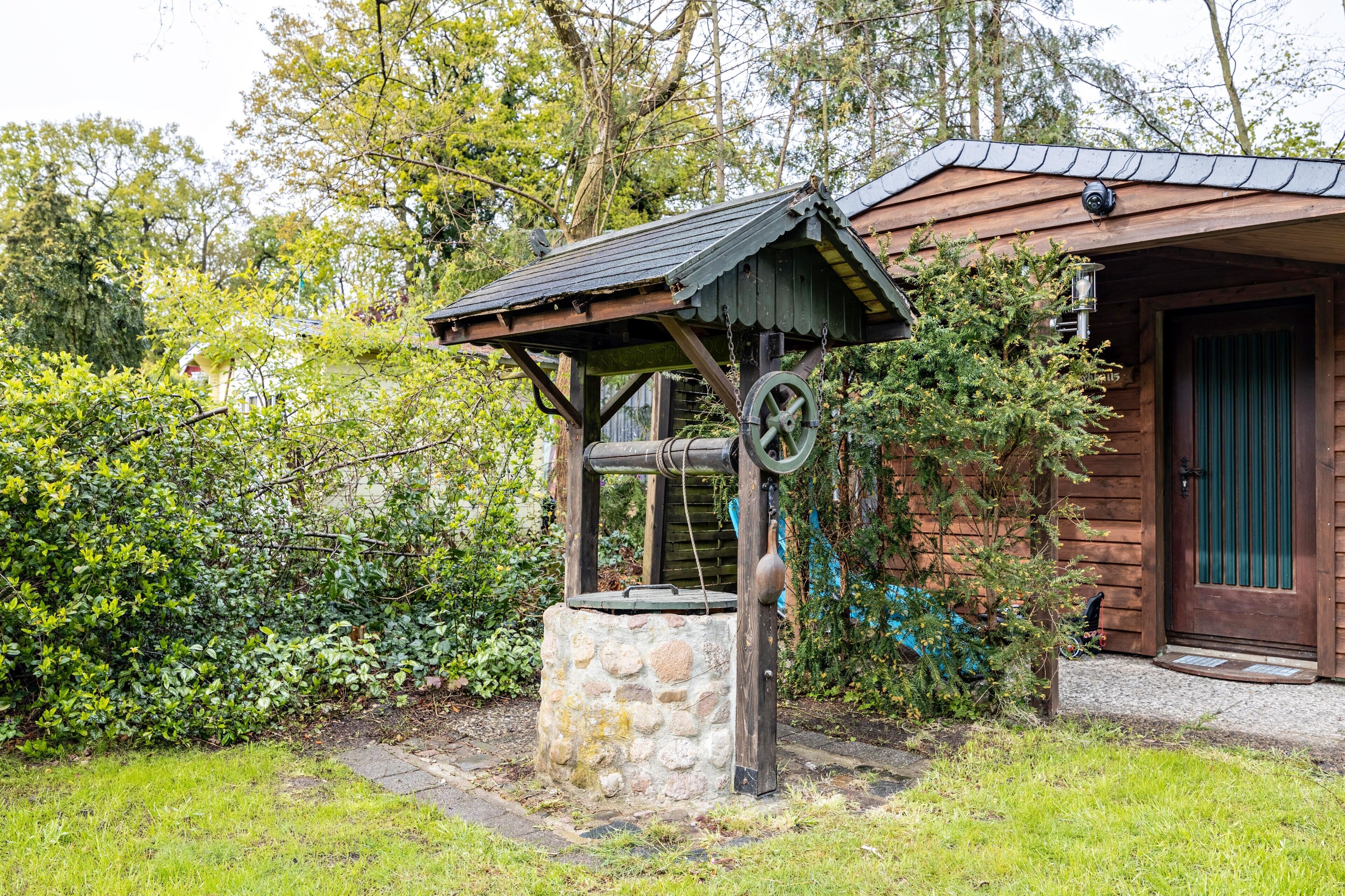 A rustic wooden structure with a stone base, a metal wheel, and a small roof.