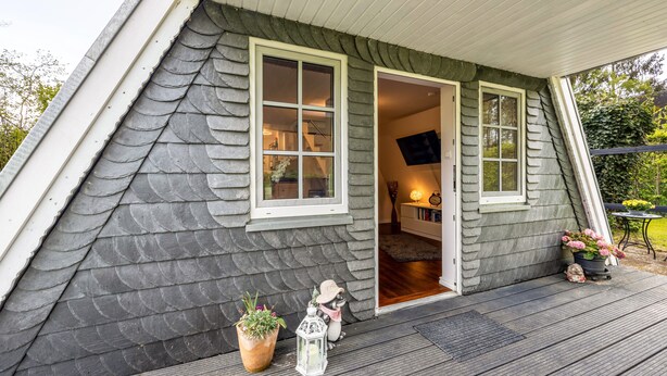 A house with a sloped roof, a door leading to an interior, and a small porch with a potted plant and a decorative lantern. - Holiday Home 'Elbliebe' with Private Terrace, Wi-Fi and Air Conditioning (Dannenberg)