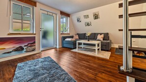 A living room with a sofa, coffee table, and a view of the outdoors through a glass door. - Holiday Home 'Elbliebe' with Private Terrace, Wi-Fi and Air Conditioning (Dannenberg)