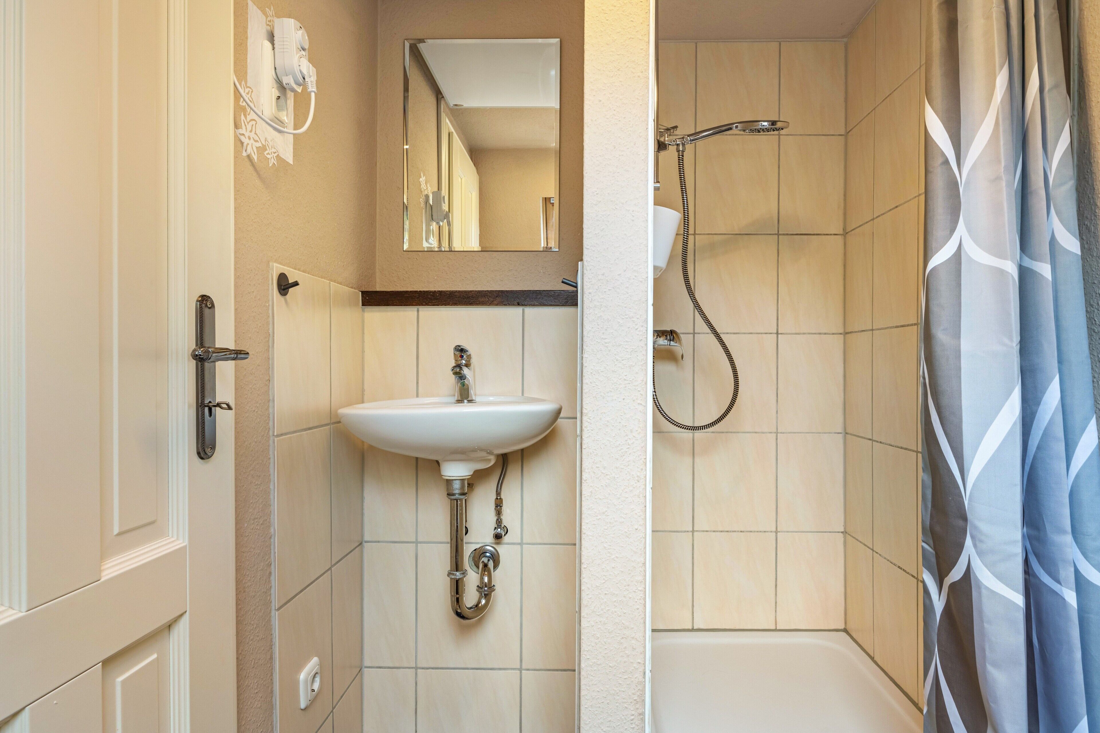 Een badkamer met een wastafel, spiegel, douche en deur.