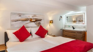 A bedroom with a bed, red pillows, a bedside table, a mirror, and a wall-mounted artwork. - Holiday flat "Emma" with mountain view, balcony and WLAN (See)