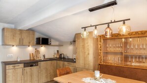 A modern kitchen with wooden cabinets, a dining table with chairs, and a wine rack. - Holiday flat "Emma" with mountain view, balcony and WLAN (See)
