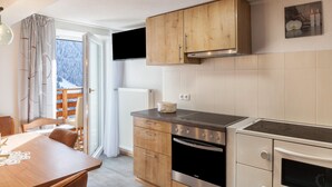 A modern kitchen with wooden cabinets, a stove, and a dining area with a table and chairs. - Holiday flat "Emma" with mountain view, balcony and WLAN (See)