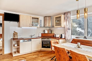 Une cuisine moderne avec des meubles en bois, un four encastré et un coin repas comprenant une table et des chaises.