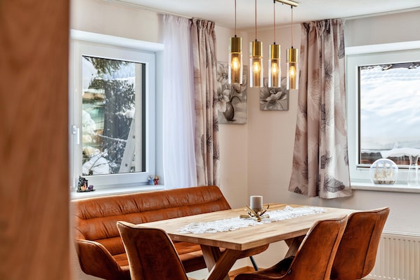 Un coin repas avec une table en bois, des chaises en cuir et une vue sur un paysage enneigé par la fenêtre.