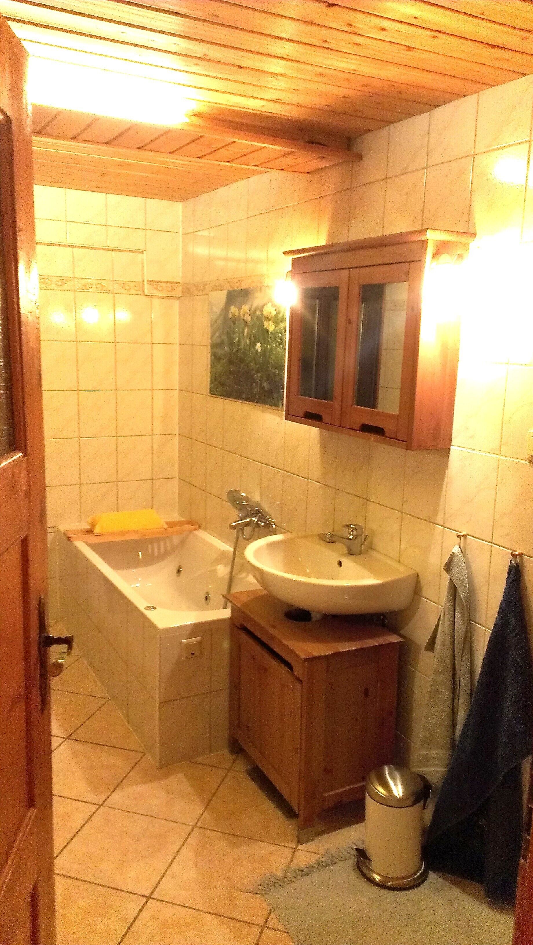 A bathroom with a bathtub, sink, wooden cabinet, and a towel rack.