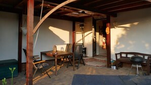 Terrassa exterior amb taula de fusta, cadires, una barbacoa i una xemeneia de obra.