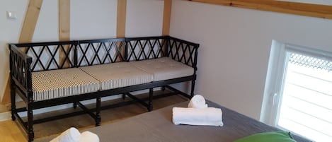 A room with a wooden ceiling, a bed with a grey mattress, two rolled towels, and a bench with a striped cushion.