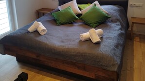 A bedroom with a wooden ceiling, a large window, a bed with green and white pillows, and a rolled towel on the bed. - Apartment 'Kleine Auszeit 1' with Private Terrace and Wi-Fi (Forst)