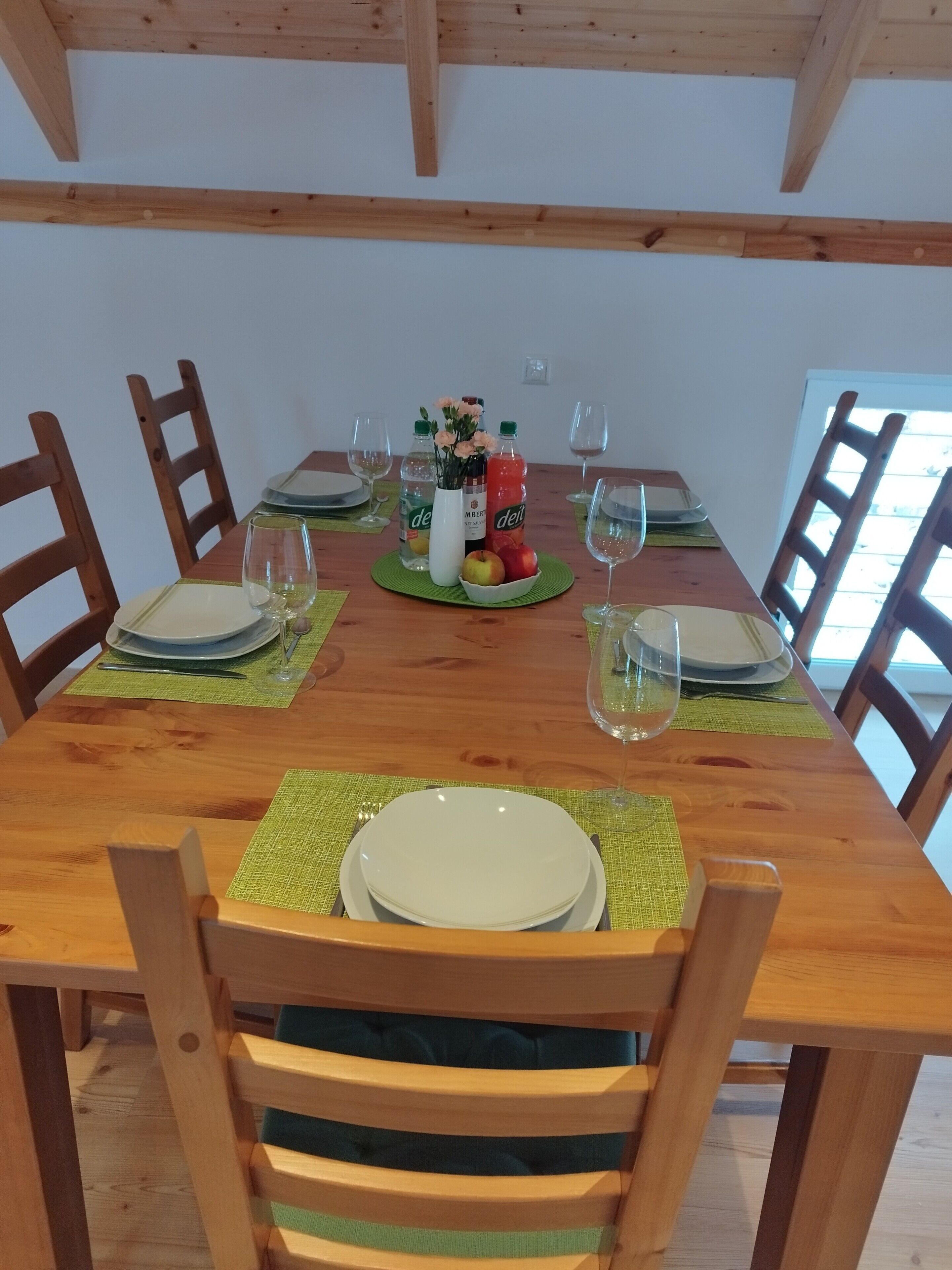 A wooden dining table set with plates, glasses, and a centerpiece of flowers and bottles.