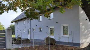 A two-story building with a grey exterior, multiple windows, and a large tree in the foreground. - Apartment 'Kleine Auszeit 1' with Private Terrace and Wi-Fi (Forst)