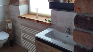 Une salle de bain avec un meuble-lavabo en bois, un lavabo blanc, une fenêtre et un mur en briques.