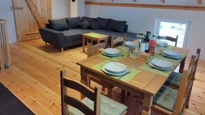 Une pièce au plancher de bois, avec une table à manger dressée pour quatre personnes, un canapé gris et une porte en bois sur laquelle est apposée une pancarte.