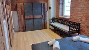 Une pièce avec un lit, un banc, une fenêtre et un mur en briques.