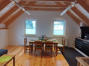 A dining area with a wooden table and chairs, two windows, a radiator, and a black appliance on the right. - Apartment 'Kleine Auszeit 2' with Private Terrace and Wi-Fi (Forst)