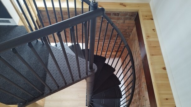 Un escalier en colimaçon avec une rampe en métal, des marches en bois et un mur en briques.