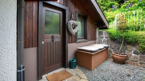 A wooden house with a brown door, a small porch with a bench, a potted plant, and a stone wall. - Holiday Home 'Amadeus Black Forest Mountain' with Mountain View, Private Terrace and Wi-Fi (Todtmoos)