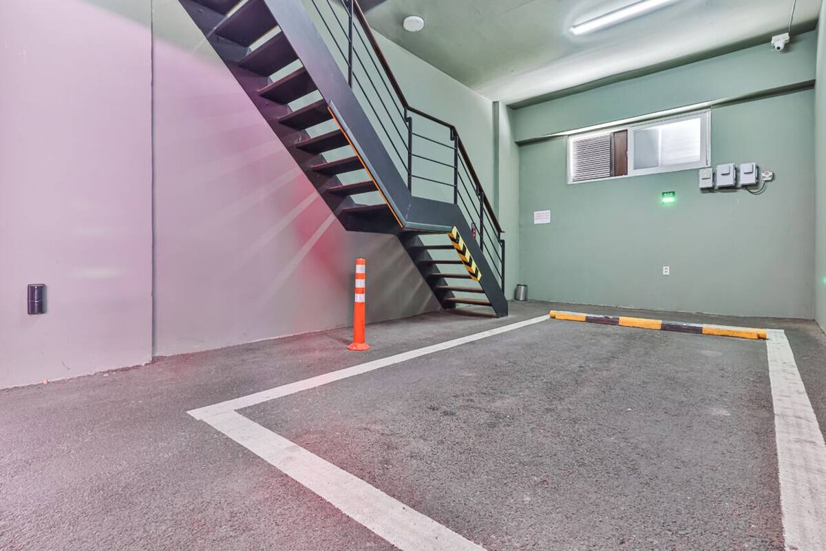 A parking garage with a staircase leading to an upper level, marked parking spaces, and a green wall with emergency equipment.