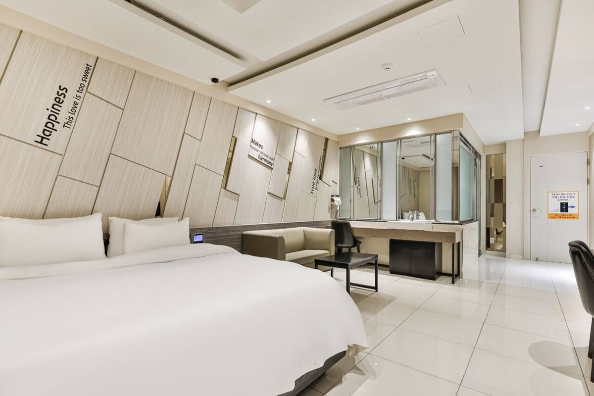 A modern hotel room with a large bed, a desk, a chair, and a mirror.