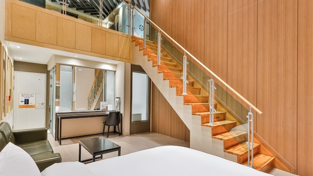 A modern hotel room with a large bed, a desk, a chair, and a staircase with wooden steps and glass railings. - Hotel A1 Jukdo (Pohang)