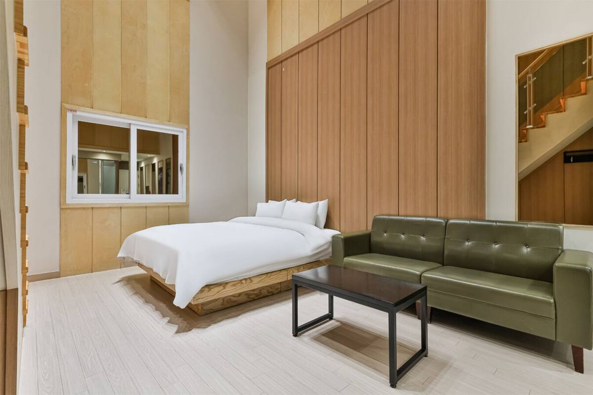 A modern room with a bed, a green sofa, a wooden wall, and a window.