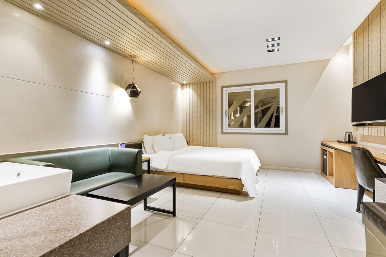 Quarto de hotel moderno com uma cama, um sofá verde, uma escrivaninha e uma televisão.