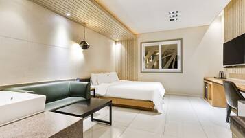 Quarto de hotel moderno com uma cama, um sofá verde, uma escrivaninha e uma televisão.