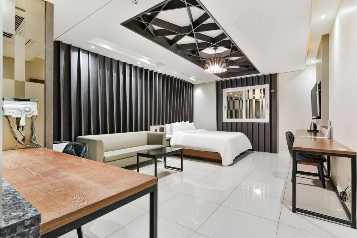A modern hotel room with a sectional sofa, a single bed, a dining table, and a TV.