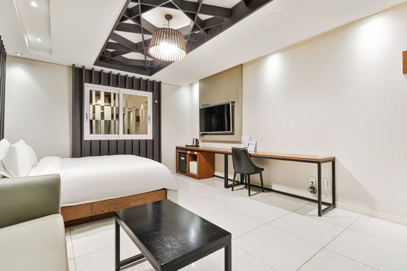 A modern hotel room with a bed, a desk, a chair, and a TV.